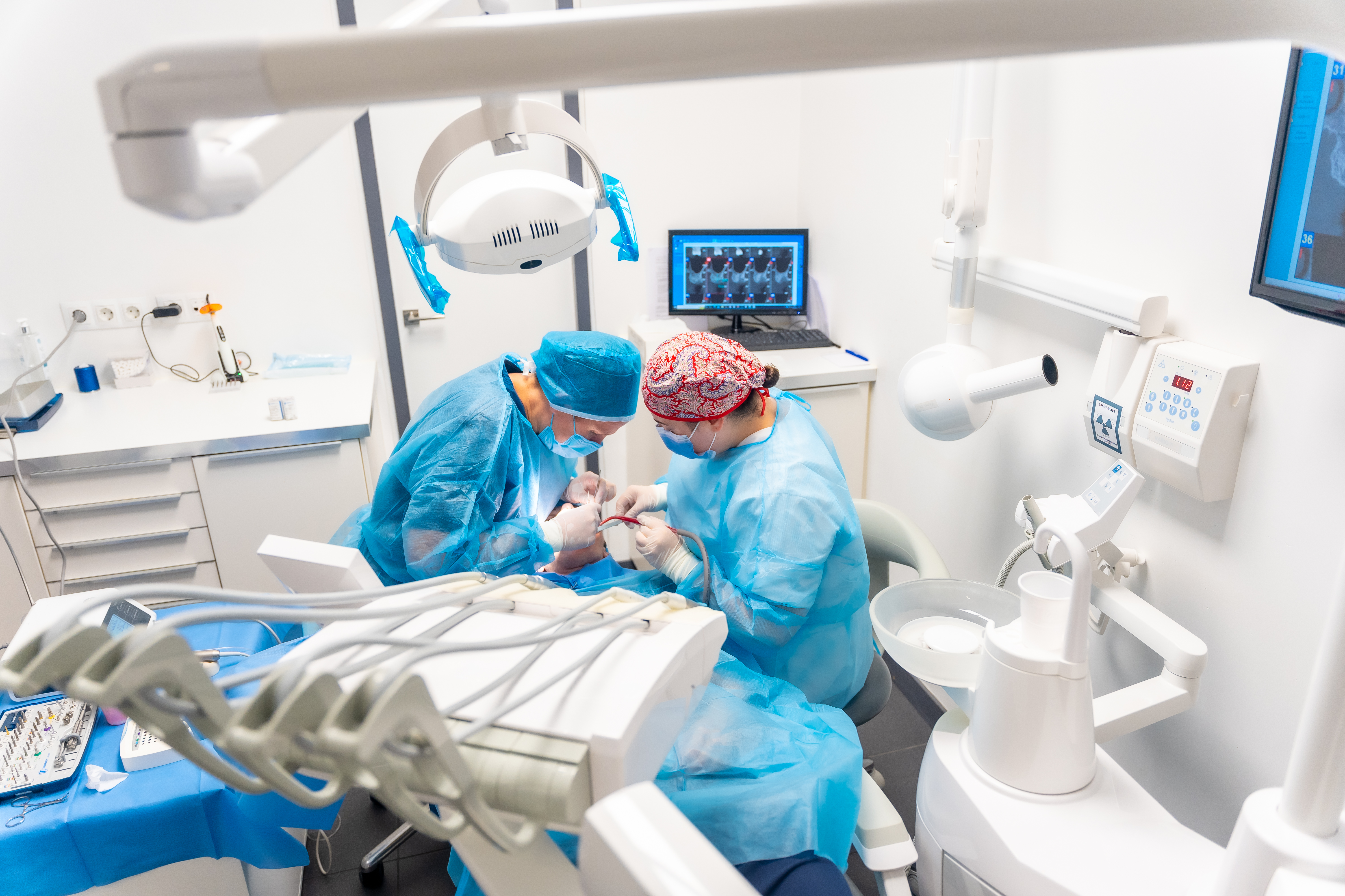 Two clinicians placing an implant, the planning scan on the monitor beside them