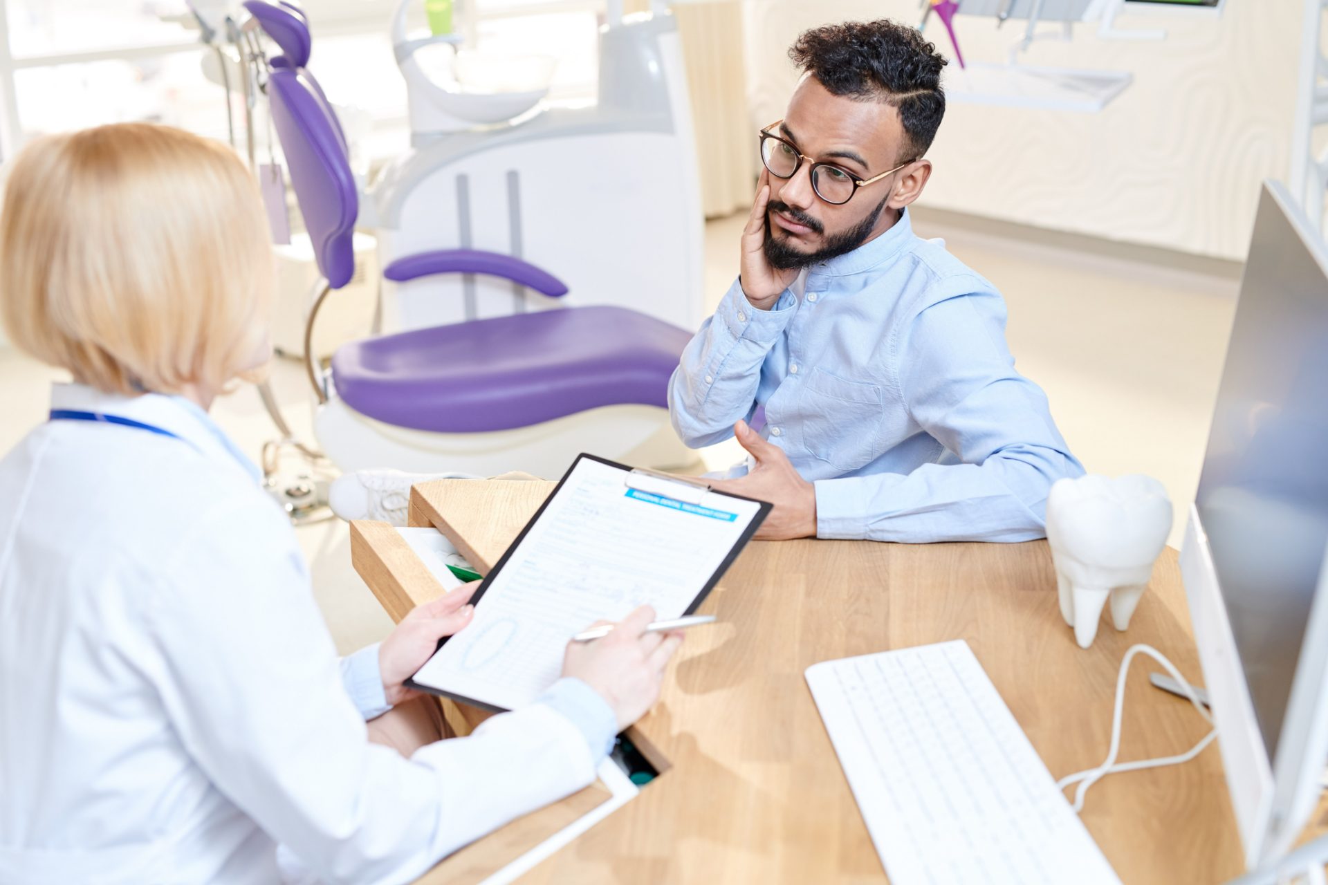 Patient holding his jaw in discomfort while a clinician reviews a treatment form with him