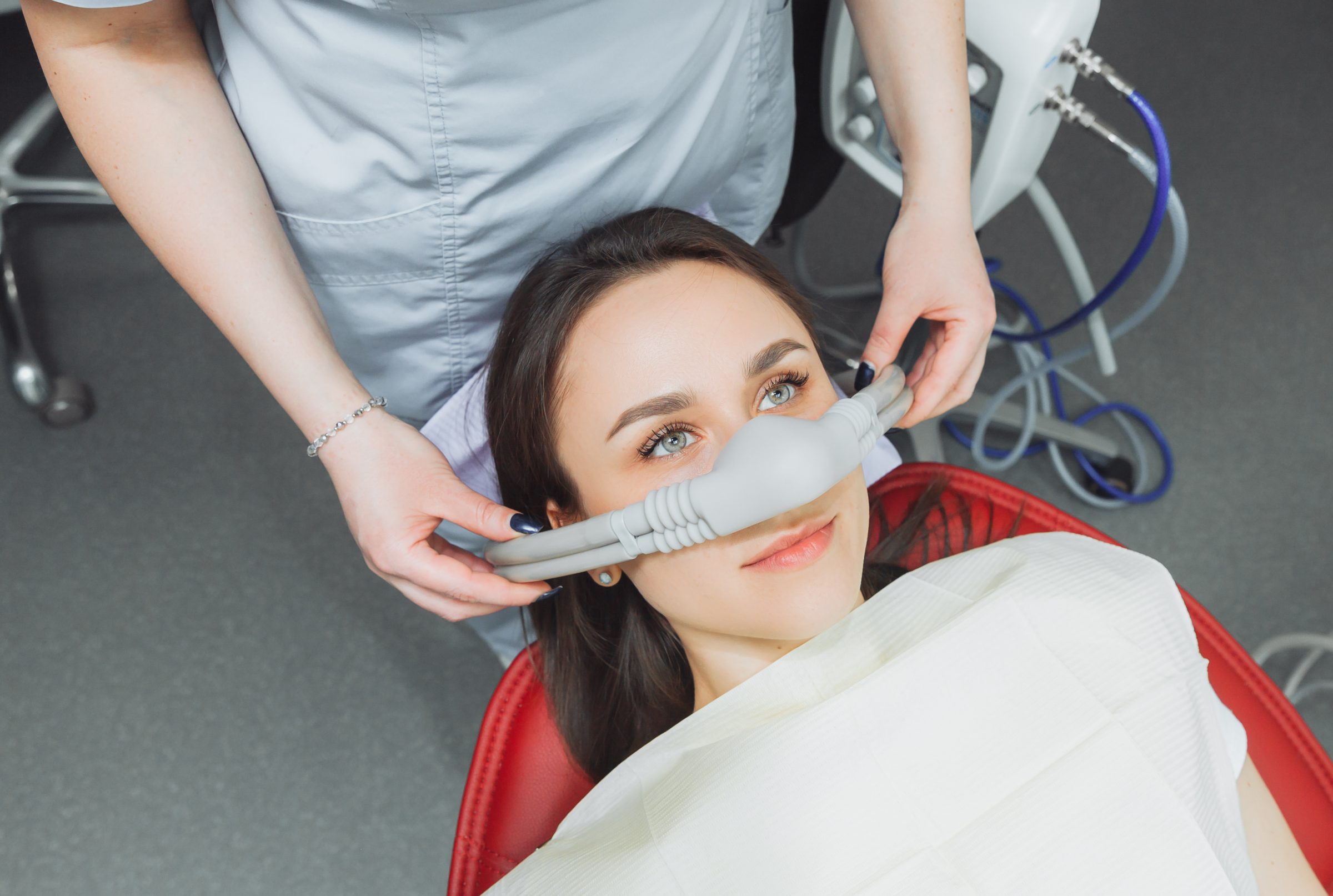 Clinician fitting a nitrous oxide nasal mask on a patient reclining in a dental chair