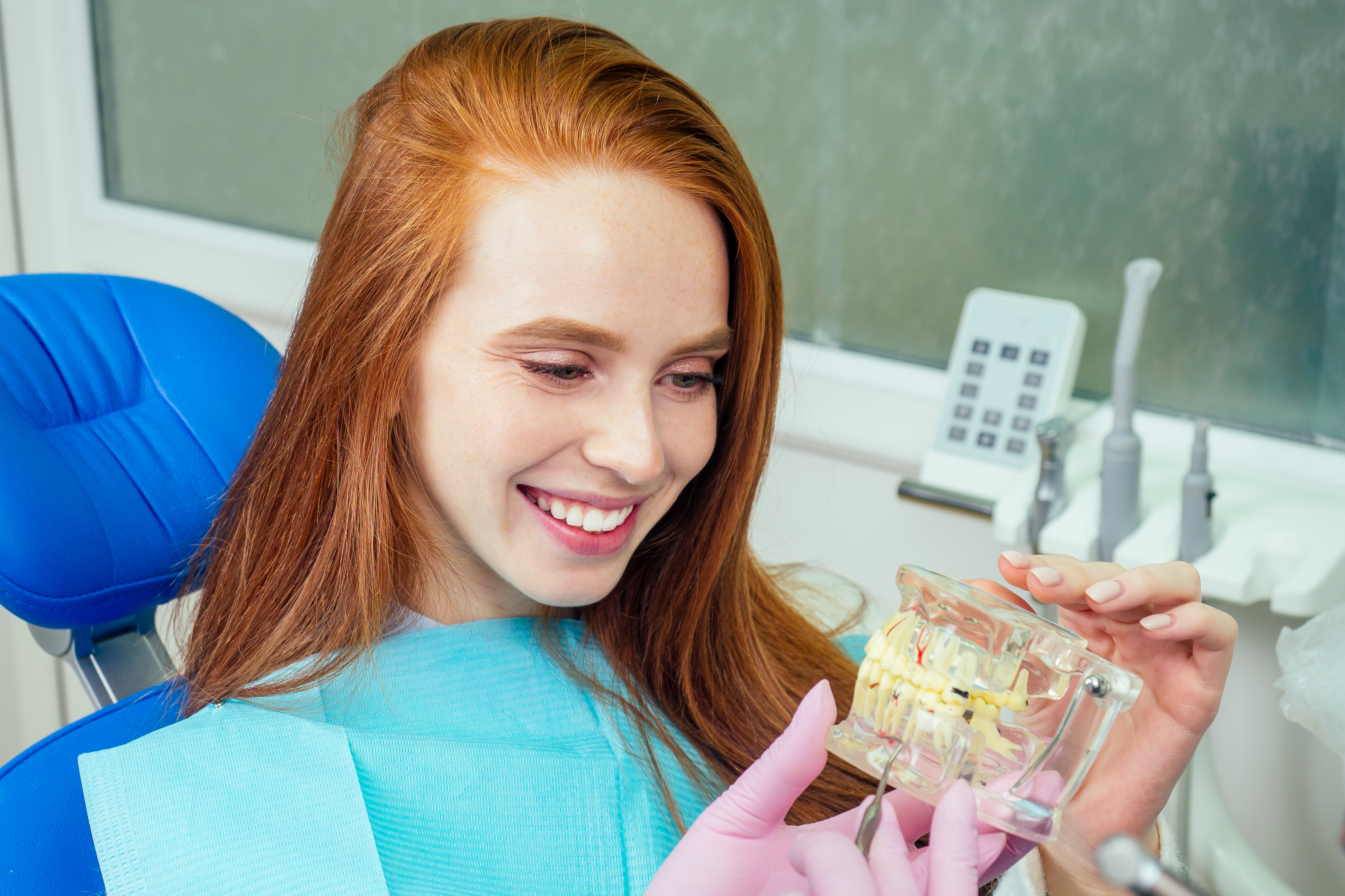 Redhaired ginger lady checking teeth in mirror at dentist office