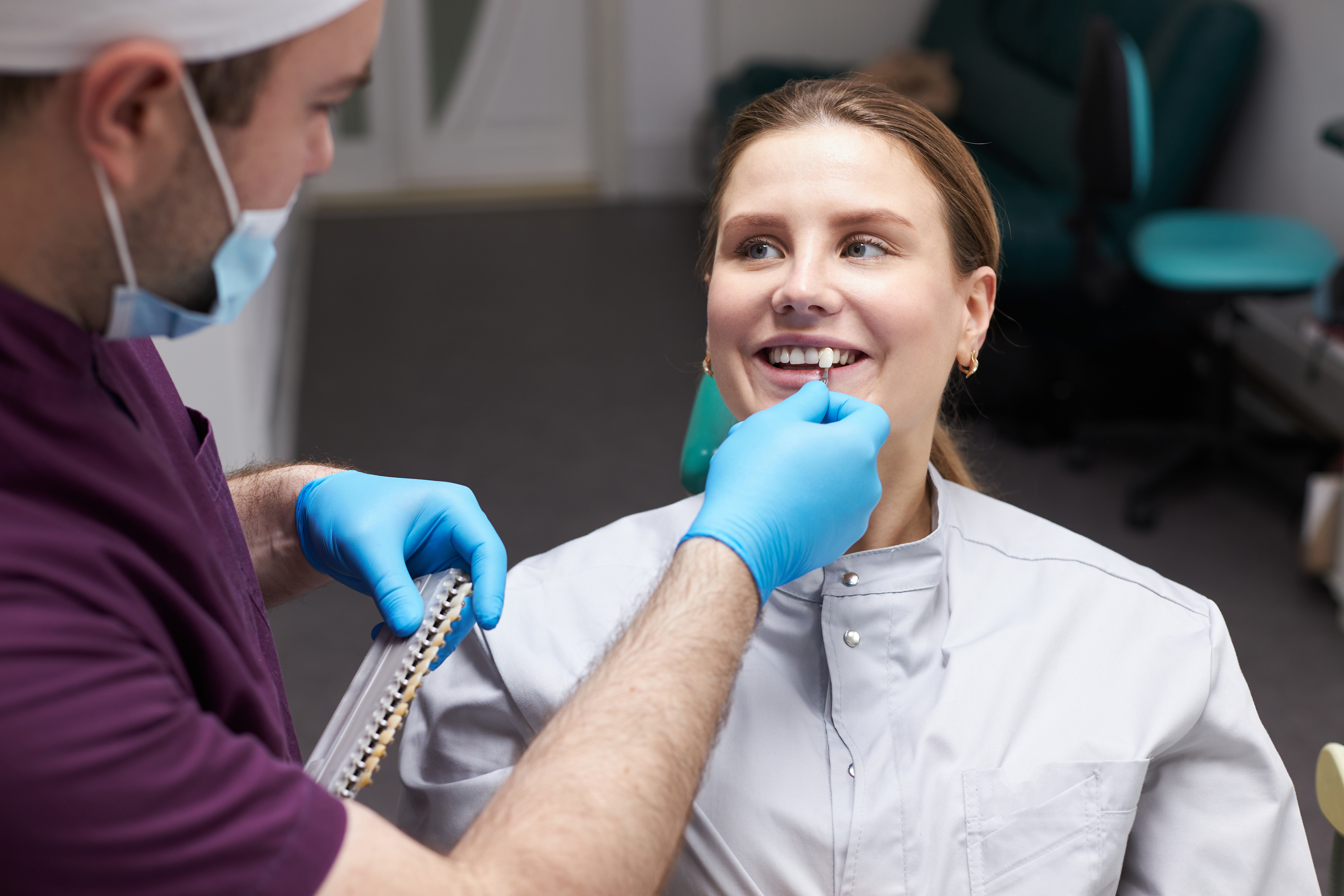 Doctor checks the color of tooth according to the comparative scale of veneers Woman at the dentist