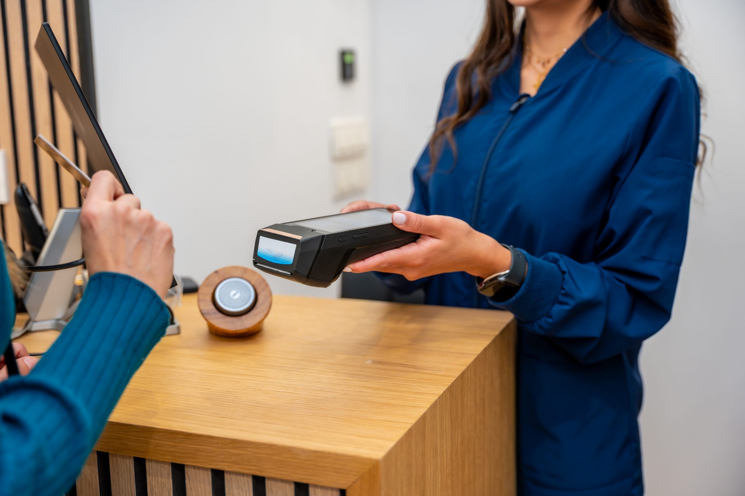 Front desk staff member holding a card payment terminal out to a patient at the counter