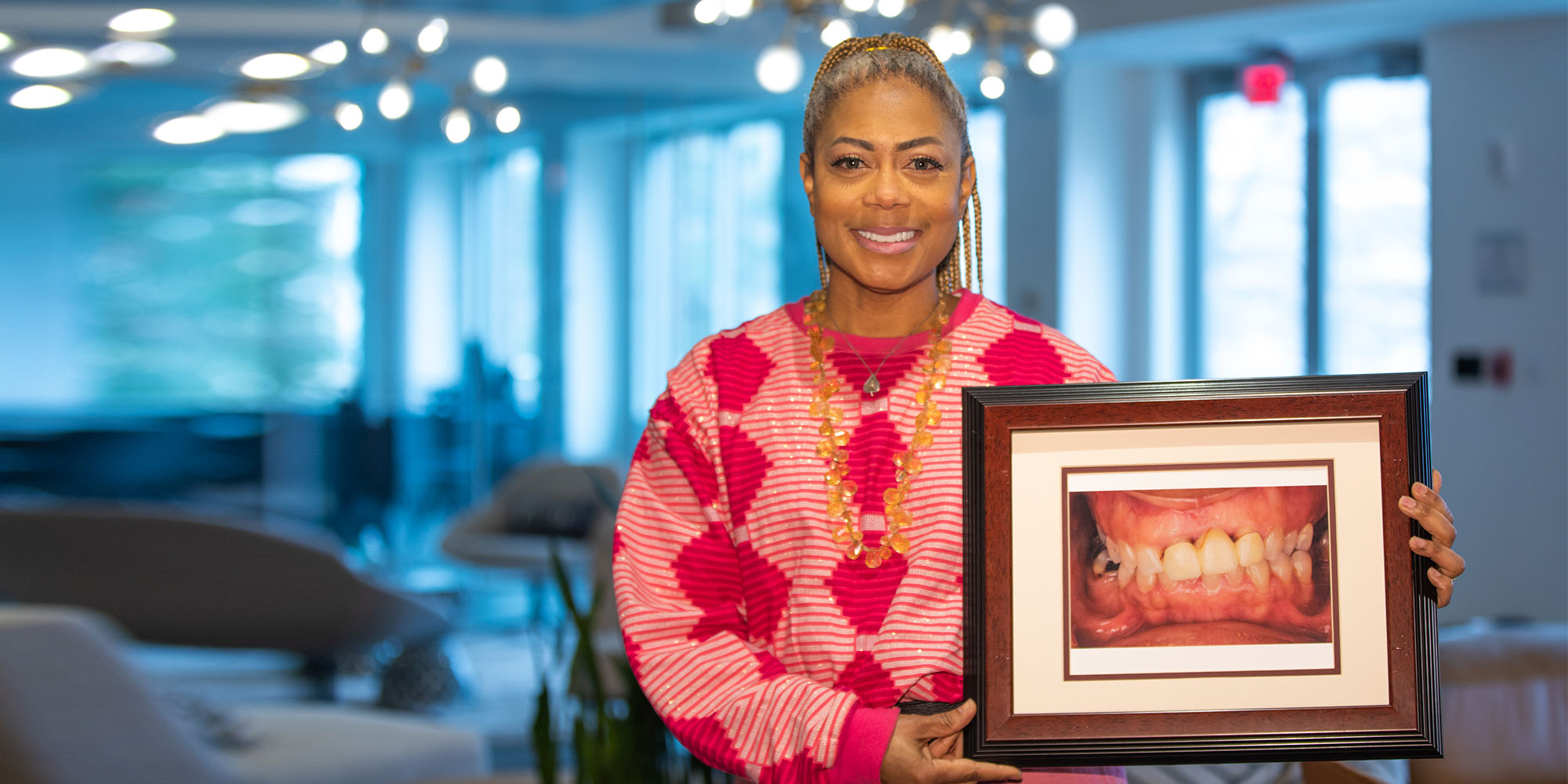 A smiling patient holding a framed photograph of her teeth before treatment